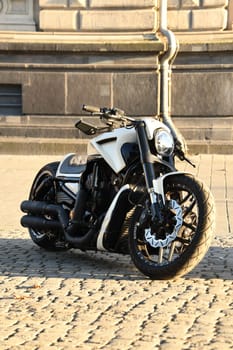 Vertical shot of a white chopper motorcycle parked under the sunlight