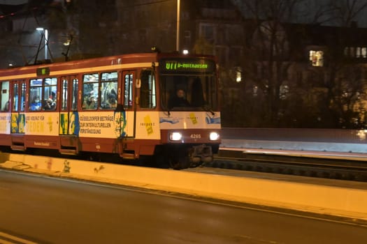A tram traveling down the track in front of buildings at night