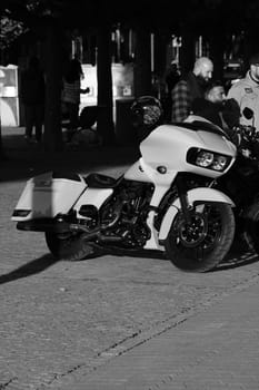 A vertical grayscale of three male standing by a white chopper motorcycle. Harley Davidon in Duesseldorf, Germany.