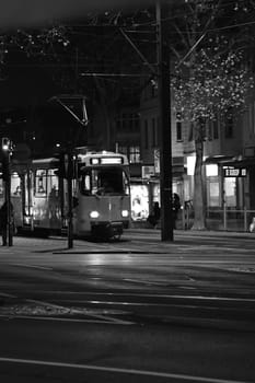 Grayscale of a tram going through town streets at night on the street