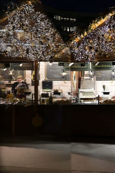 Christmas market stall reflected in a glass facade with people sitting near
