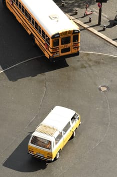 Vertical shot of a yellow and white automobile driving behind an American school bus on a roadway