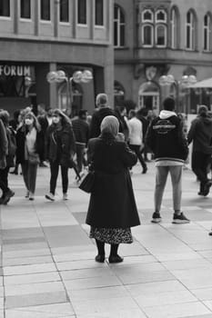 Vertical grayscale of a woman wearing a hijab standing in front of Cologne Cathedral, Germany