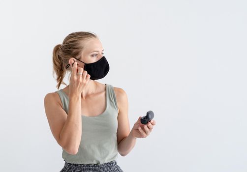 Music, isolation and leisure. Young woman in a protective mask holding wireless earbuds