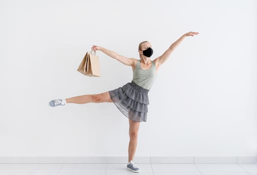 Healthcare and quarantine concept. Young woman dancing ballet with shopping bags in a protective mask. Shopping in isolation and quarantine