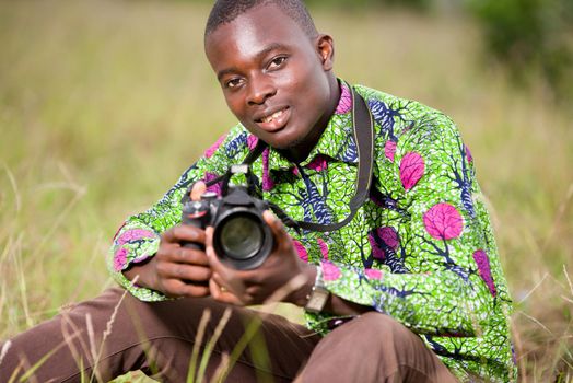 portrait of smiling tourist photographer sitting in the grass and holding a professional camera.