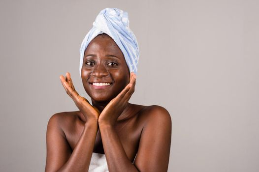young woman standing on gray towel tied on head with hands under chin.and smiles.