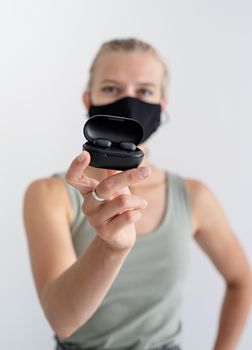 Music, isolation and leisure. Young woman in a protective mask holding wireless earbuds