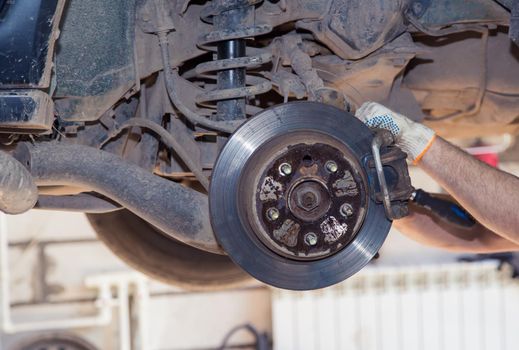 The gloved hands of a man dismantle the worn out rear wheel hub caliper. In the garage, a person changes the failed parts on the vehicle. Small business concept, car repair and maintenance service.