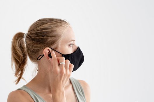 Music, isolation and leisure. Young woman in a protective mask holding wireless earbuds