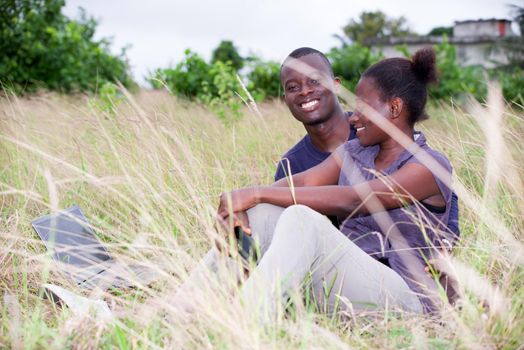 happy young couple in love relaxes sitting in the grass in summer. Positive man and a woman having fun enjoying the outdoors and nature.