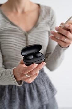 Wireless technology. Young woman holding wireless earbuds operated by the phone