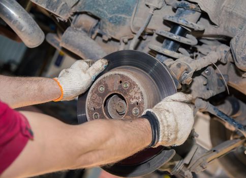 The man's hands remove the worn and rusty rear brake disc. In the garage, a person changes the failed parts on the vehicle. Small business concept, car repair and maintenance service.