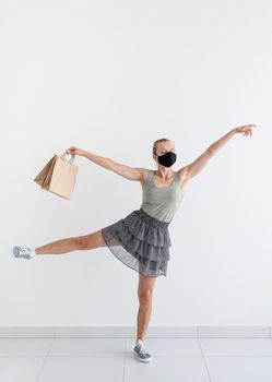 Healthcare and quarantine concept. Young woman dancing ballet with shopping bags in a protective mask.