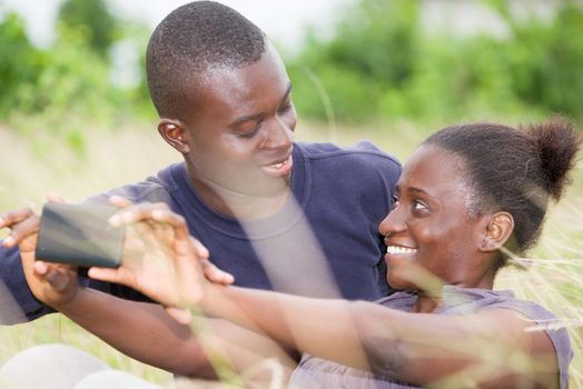 concept of love and people - happy teenage couple lying on the grass and taking picture on smart phone in summer.