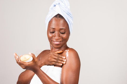 beautiful smiling african woman putting ointment on her body after her bath.