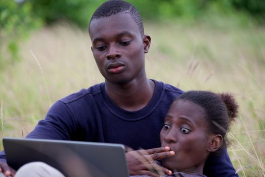young african couple sitting in the grass with laptop.