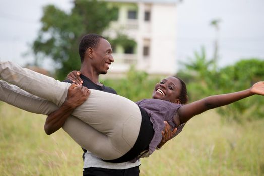 Shot of young woman carrying her boyfriend in a field of grass. Couple having fun during their summer vacation.