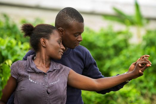 young african couple standing in a park smiling, embracing.