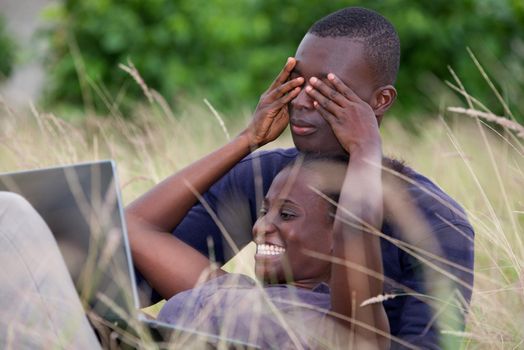 concept of love and people - happy teenage couple lying on the grass in front of a laptop, laughing and sharing moments of happiness while looking on smart phone in the summer.