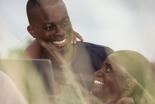 young african couple sitting in the grass with laptop smiling.