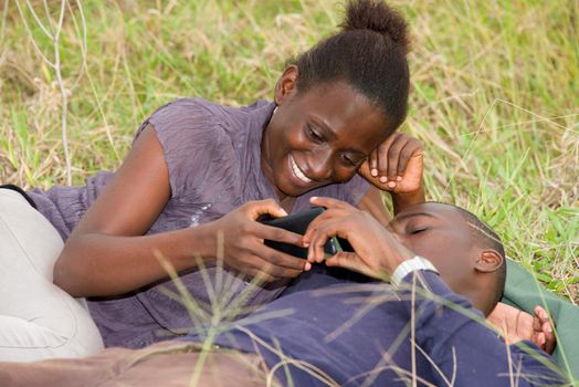 Happy couple lying on green grass laughing and smiling while using mobile phone.