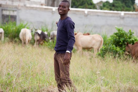 young farmer standing in the grass smiling and happy shows the cattle grazing and looking at the camera