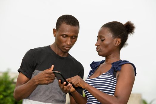 portrait of young african couple standing staring at mobile phone.