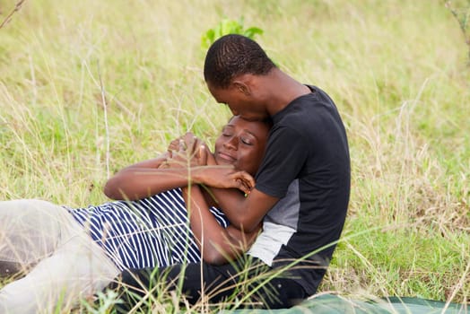 young african couple sitting in a park, intertwined.