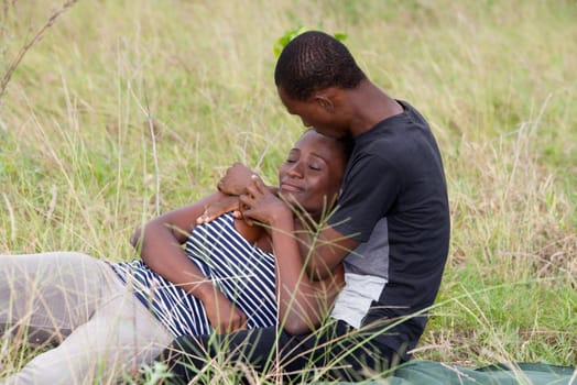 young african couple sitting in a park, intertwined.