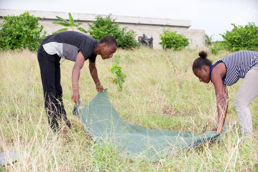 young african couple trying to spread a blanket in a park.