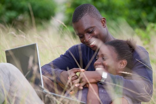 concept of love and people - happy teenage couple lying on the grass in front of a laptop, laughing and sharing moments of happiness while looking on smart phone in the summer.