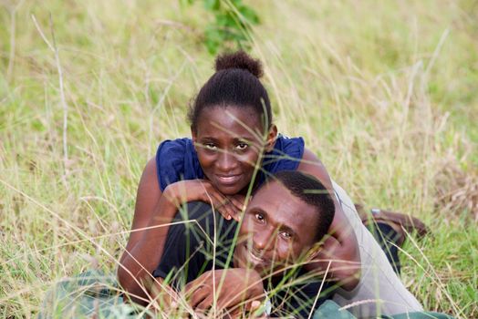 young african couple lying in the grass smiling on the camera.
