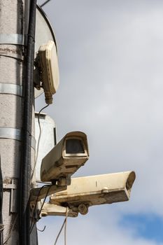 two old security surveillance cameras on street light pole on blue sky background.