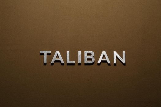 the word taliban laid with silver metal letters on tan khaki canvas fabric