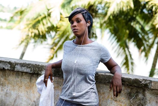 sporty woman leaning against a wall, looking on her phone while listening to music, takes a break in the air after a morning run