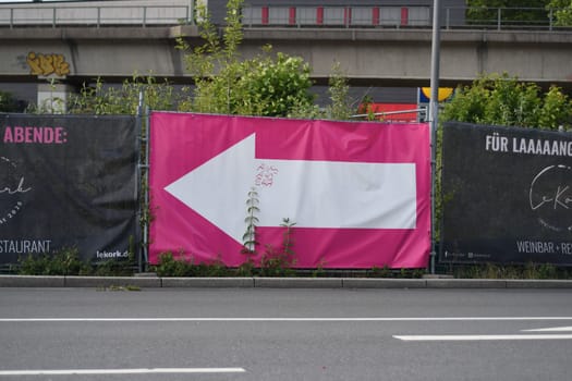 Billboard with a pink poster and a white arrow pointing left