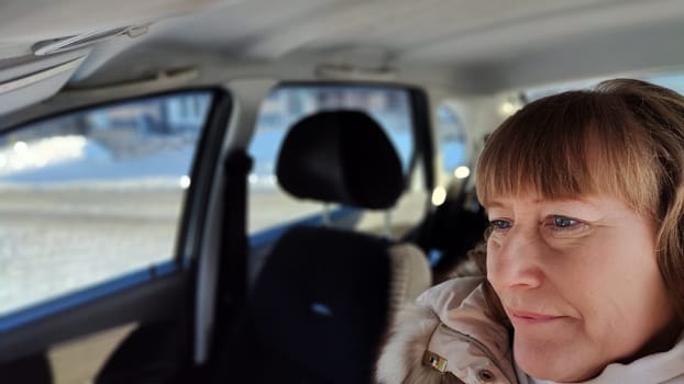 Woman sitting in the car in road trip. Blonde senior Woman driving transport. Lady travelling in cold time