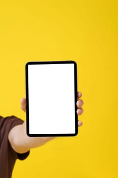 close-up image of a man's hand holding a blank screen Tablet PC against a yellow background, showcasing technology concept and digital revolution. Copy Space concept for advertising. . High quality photo