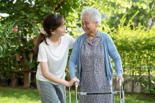 Caregiver help Asian elderly woman patient walk with walker in park, healthy strong medical concept.