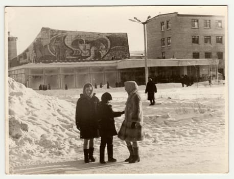 USSR - CIRCA 1980s: Vintage photo shows girls and boy talk on street in winter. Socialist mosaic on background.