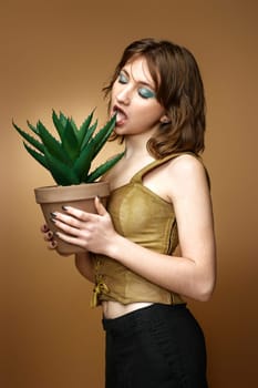 young woman with stylish hairstyle posing with plant in pot on beige background.