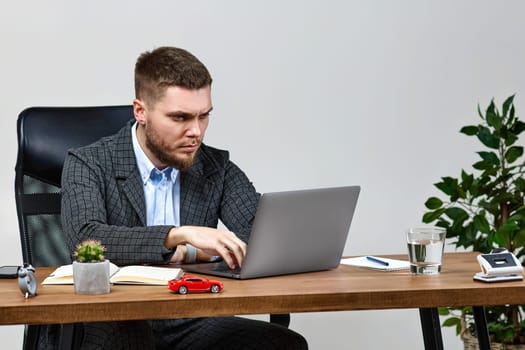 young bearded businessman typing on computer keyboard, sending emails to business partners, sitting on chair at desk
