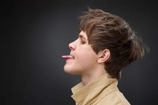 side view of caucasian man with hairstyle in coat showing the tongue on black background. fashion modern style look