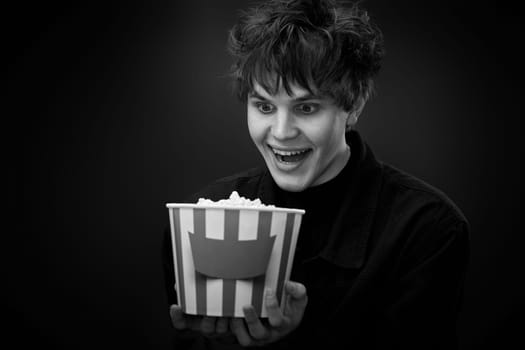 portrait of crazy young man holding bucket of popcorn and grimacing . black and white