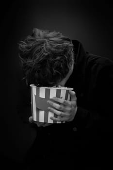 portrait of crazy young man holding bucket of popcorn and grimacing . black and white