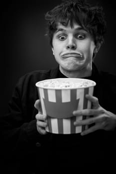 portrait of crazy young man holding bucket of popcorn and grimacing . black and white