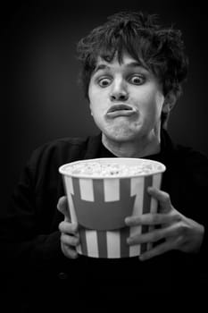 portrait of crazy young man holding bucket of popcorn and grimacing . black and white