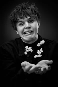 portrait of crazy young man throwing up popcorn and grimacing . black and white