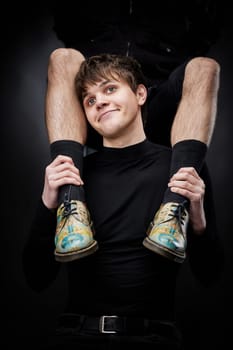 young handsome guy hugs male legs in bright shoes on black background. fashion